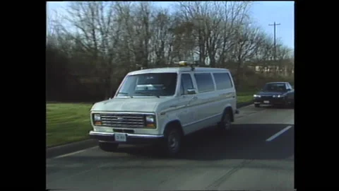 1990s: White van drives down road. Rack on roof of car holds camera and Stock Footage 144700986