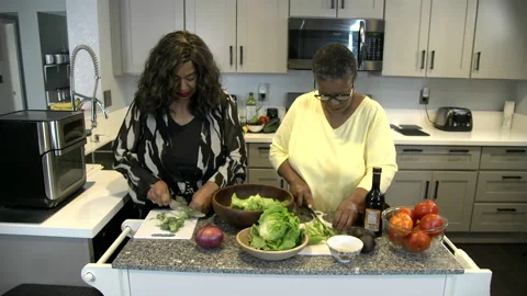 2 African american ladies in kitchen preparing salad cutting onion Stock Footage