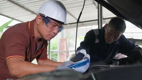 2 auto mechanics working and checking the repair work on a car at a car garage Stock Footage 246118652