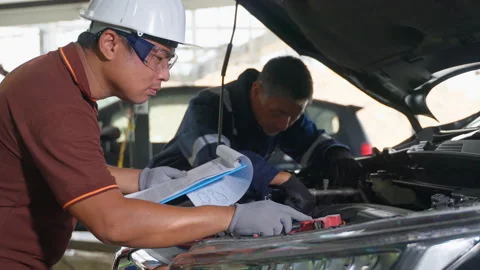 2 auto mechanics working and checking the repair work on a car at a car garage Stock Footage 246122280