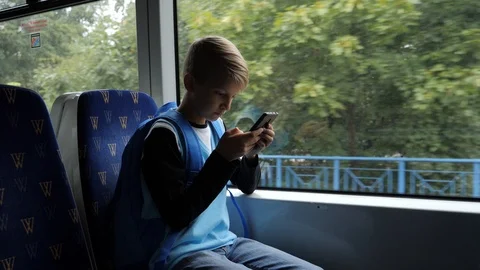 2 Boy going to school by tram sit and use type his smartphone in transport by Stock Footage 94613262