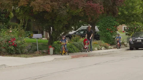 2 Boys Ride Bikes With Mom Pushing Baby in Stroller Stock Footage 62652720