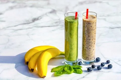 2 different kind of banana based smoothies with ingredients on marble table b Stock Photos