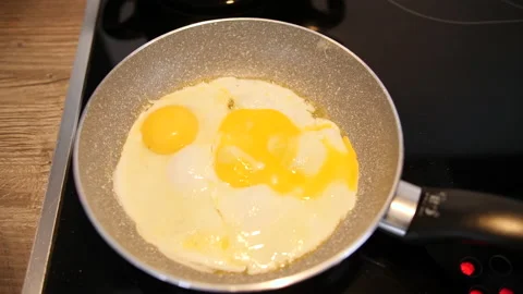 2 fried eggs, not perfectly shaped, being cooked in a small pan Stock Footage 231931455