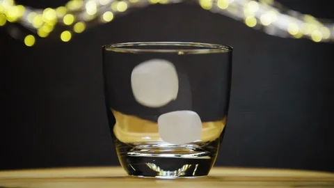 2 ice cubes dropped into empty glass and rotates Stock Footage 128425365