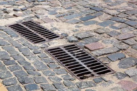 The 2 iron grates of the drainage system hatch on the road paved. Stock Photos