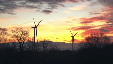 2 large wind turbines turning in a field next to lake with deep orange sunset Video stock 146268869