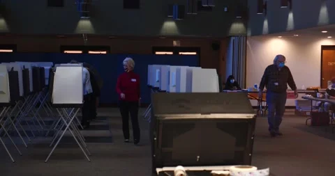 2 masked poll workers walk towards camera as masked people vote in background Stock Footage 152520645