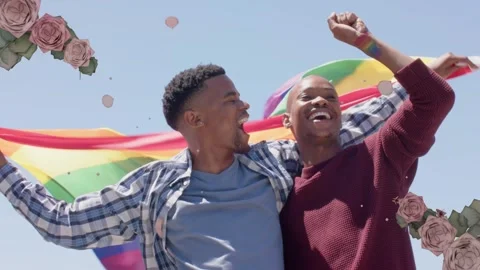 2 men cheering with breeze billowing rainbow flag, floral confetti around them Stock Footage 340654626
