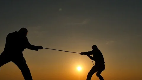 2 men competition with rope pulling silhoettes with sun on horizon Stock Footage 89825835