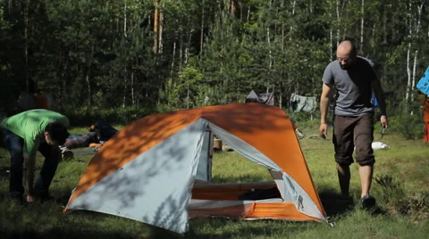 2 men stacked orange tent. Summer sunny day in the forest Stock Footage 64486916