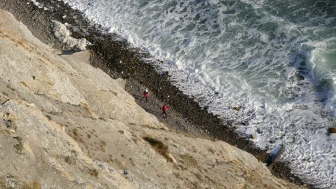 2 people in red are walking along the coast and are hidden from view behind the Stock Footage 97398963