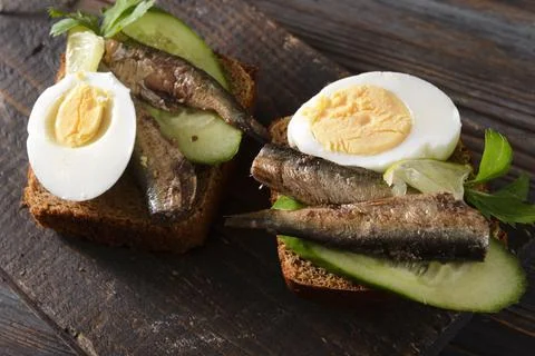 2 sandwiches with sprats, boiled egg and cucumber on a dark wooden background Stock Photos