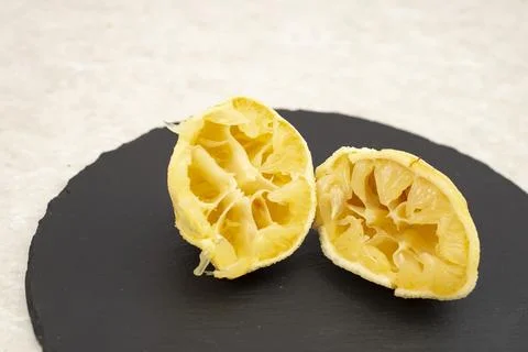 2 squeezed lemon halves on a round black stone tile, Stock Photos