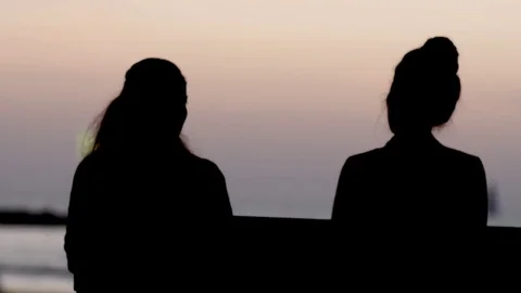 2 woman talking on bench looking at sunset at the sea beach view Stock Footage 75397165