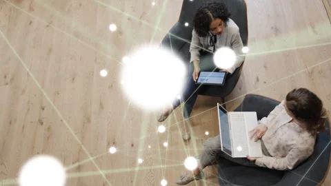 2 women tapping tablet and scrolling laptop in office creating tech network Stock Footage 333494251
