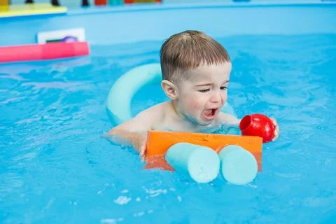 A 2-year-old boy learns to swim in a pool with a coach. Swimming lessons fo.. Stock-Fotos