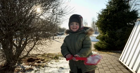 2-Year-Old Boy Plays with Toy Shovel in Snow, Runs Around Corner of House Stock Footage 240357571