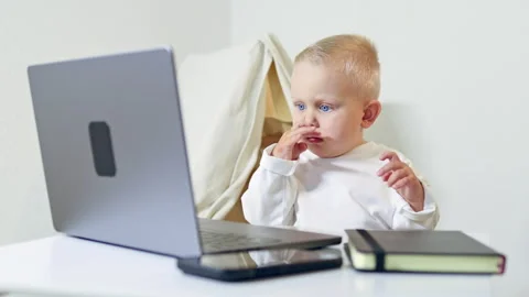 A 2-year-old boy sits at home at a table and looks at a laptop. A child watches Stock Footage 315528765