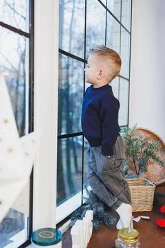 A 2-year-old boy sits by the window in the New Year. New Year's atmosphere .. Stock Photos