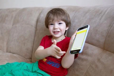 2 year old boy is sitting on the couch and playing on the phone. Little cute boy Stock Photos