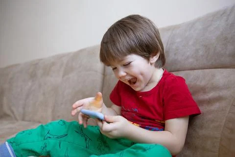 2 year old boy is sitting on the couch and playing on the phone. Little cute boy 写真素材