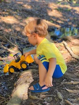 2 year old child playing with tractor on land and in water. Stock Photos