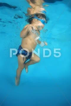 2 years boy in a swimming goggles learning to swim underwater in the pool Stock Photos