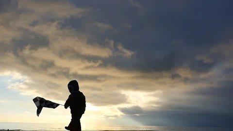 2 years old boy waing with flag silhouette at the sea shore Stock Footage 100717347