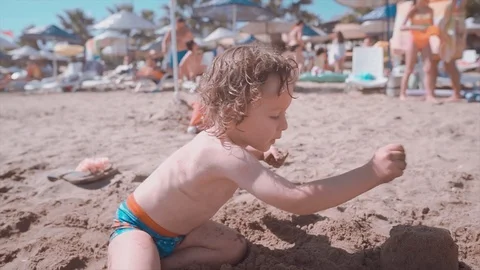 2 years old long haired boy is playing with sand on beach, summertime. Video stock 112287679
