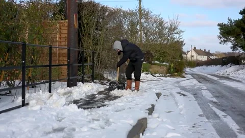 A 20 something man clearing the pavement after heavy snow in the UK Stock Footage 163091114