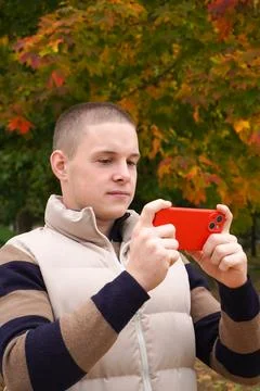 20-year-old positive guy is looking at the smartphone screen in a red case Stock Photos