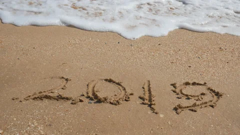 2019 drawn on the sand being washed away by a wave at the beach Stock Footage 115445101