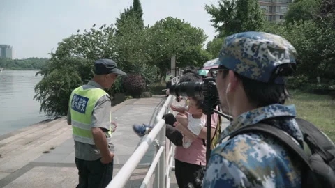 2019 Jun 10, Jiaxing. Security staff and photographers by lakeside walkway Stock Footage 338278402