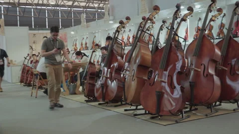 2019 Oct 13, Shanghai. Visitors browse polished string instruments displayed Stock Footage 345928524