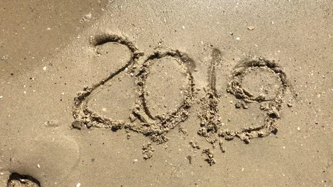 2019 year drawn on the sand being washed away by a wave on the beach Stock Footage 115777841