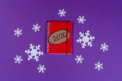 2020 bubble on the red notebook, white snowflakes on the violet background. Stock Photos