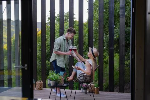 A young couple clinking with wine outdoors, weekend away in tiny house in countryside, sustainable living. xkwx love, wine, couple, woman, man, outdoor, happy, terrace, romance, romantic, together, young, drink, glass, person, smiling, caucasian, celebration, lifestyle, garden, party, relationship, two, alcohol, cheerful, vacation, tourism, closeness, date, honeymoon, newlyweds, lover, positive, togetherness, drinking, champagne, evening, holding, tiny house, holiday, nature, off beat, relax, meditation, digital detox, candle, hygge, travel, weekend away