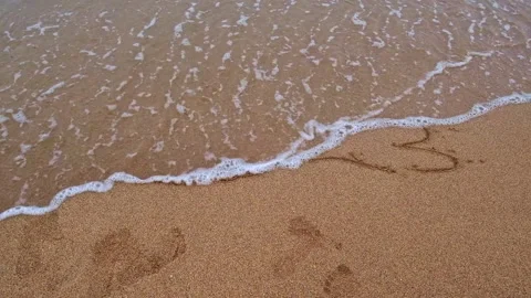 2023 is washed away by a wave. The numbers 2023 are drawn on the sand on the Stock Footage 235316409