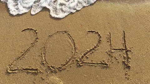 2024 written in sand on the beach with ocean waves washing over Stock Footage 282103695