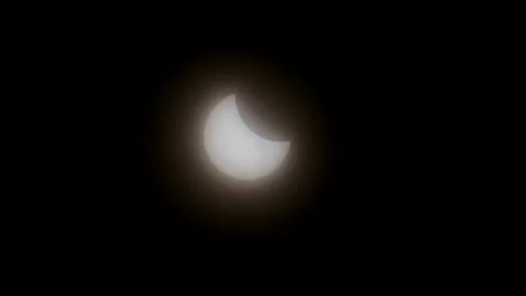 2025 Solar eclipse moon shadow passing the sun as clouds pass fast in front Stock Footage 305642319