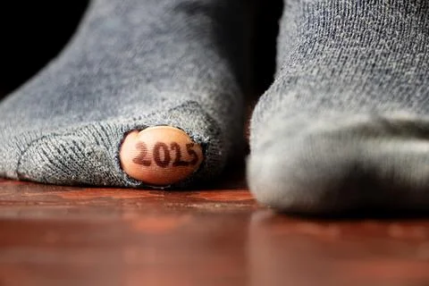 2025 written on a toe and the toe sticks out of a hole in a torn sock on th.. Stock Photos