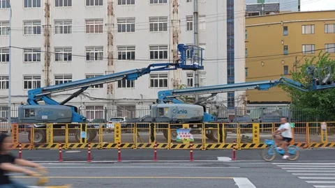 2026 Aug 28, Shanghai. Cyclists and car pass blue construction boom lifts Vidéo 344853022