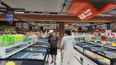 2026 Jul 04. Shoppers Browsing Frozen Food Aisles in Modern Supermarket Stock Footage 339086503