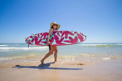 A Hispanic woman wearing swimwear while holding a surfboard on the beach xkwx attractive, beach, coast, female, girl, happy, hispanic, holiday, leisure, lifestyle, ocean, people, person, pretty, sand, sea, summer, surf, swim, vacation, voard, water, wear, woman, young