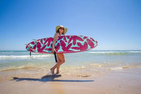 A Hispanic woman wearing swimwear while holding a surfboard on the beach xkwx attractive, beach, coast, female, girl, happy, hispanic, holiday, leisure, lifestyle, ocean, people, person, pretty, sand, sea, summer, surf, swim, vacation, voard, water, wear, woman, young