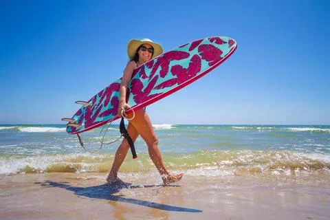 A Hispanic woman wearing swimwear while holding a surfboard on the beach xkwx attractive, beach, coast, female, girl, happy, hispanic, holiday, leisure, lifestyle, ocean, people, person, pretty, sand, sea, summer, surf, swim, vacation, voard, water, wear, woman, young