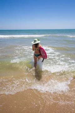 A Hispanic woman wearing swimwear while holding a surfboard on the beach xkwx attractive, beach, coast, female, girl, happy, hispanic, holiday, leisure, lifestyle, ocean, people, person, pretty, sand, sea, summer, surf, swim, vacation, voard, water, wear, woman, young