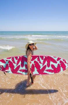 A Hispanic woman wearing swimwear while holding a surfboard on the beach xkwx attractive, beach, coast, female, girl, happy, hispanic, holiday, leisure, lifestyle, ocean, people, person, pretty, sand, sea, summer, surf, swim, vacation, voard, water, wear, woman, young