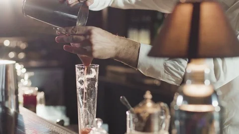 20s Bartender in a hat is pouring mixed cocktail from shaker in a glass Stock Footage 75232290